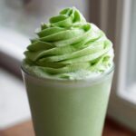 A vibrant green Copycat Shamrock Shake topped with a tall swirl of mint whipped cream.