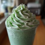 Close-up of a vibrant green Copycat Shamrock Shake topped with a generous swirl of mint whipped cream.