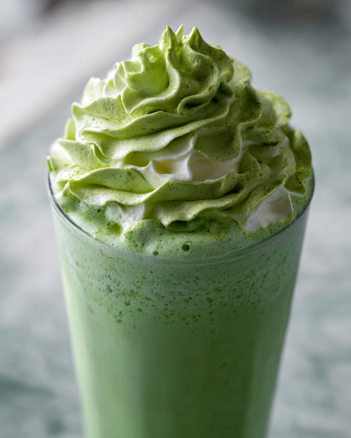 Close-up of a vibrant green Copycat Shamrock Shake topped with swirled mint whipped cream.