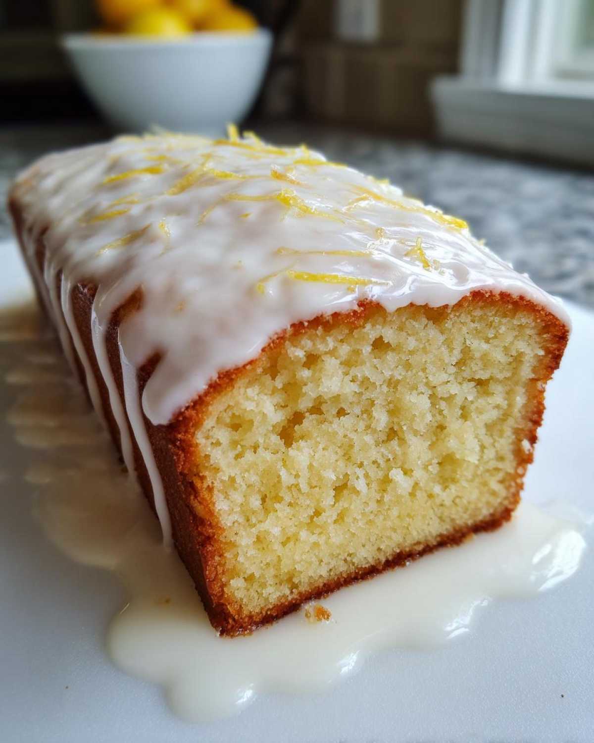 Close-up of a freshly baked Copycat Starbucks Iced Lemon Loaf with thick white glaze and lemon zest topping.