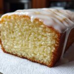 Close-up of a slice of moist Copycat Starbucks Iced Lemon Loaf with thick white glaze dripping down the side.