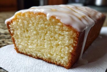 Close-up of a slice of moist Copycat Starbucks Iced Lemon Loaf with thick white glaze dripping down the side.