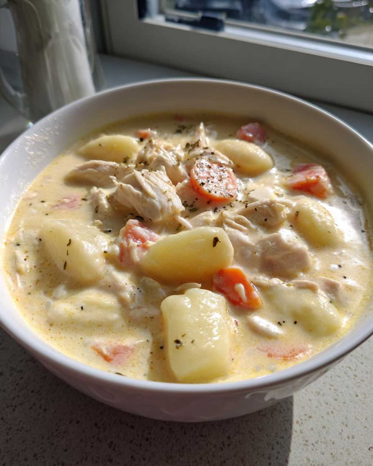 Close-up of a white bowl filled with Creamy Chicken Gnocchi Soup, featuring tender chicken, soft gnocchi, and carrots.