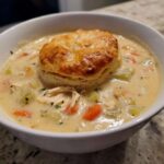 A bowl of creamy Chicken Pot Pie Soup filled with vegetables and topped with a golden baked biscuit.