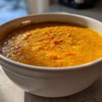 Close-up of a white bowl filled with vibrant orange Creamy Coconut Lentil Soup, topped with black pepper.