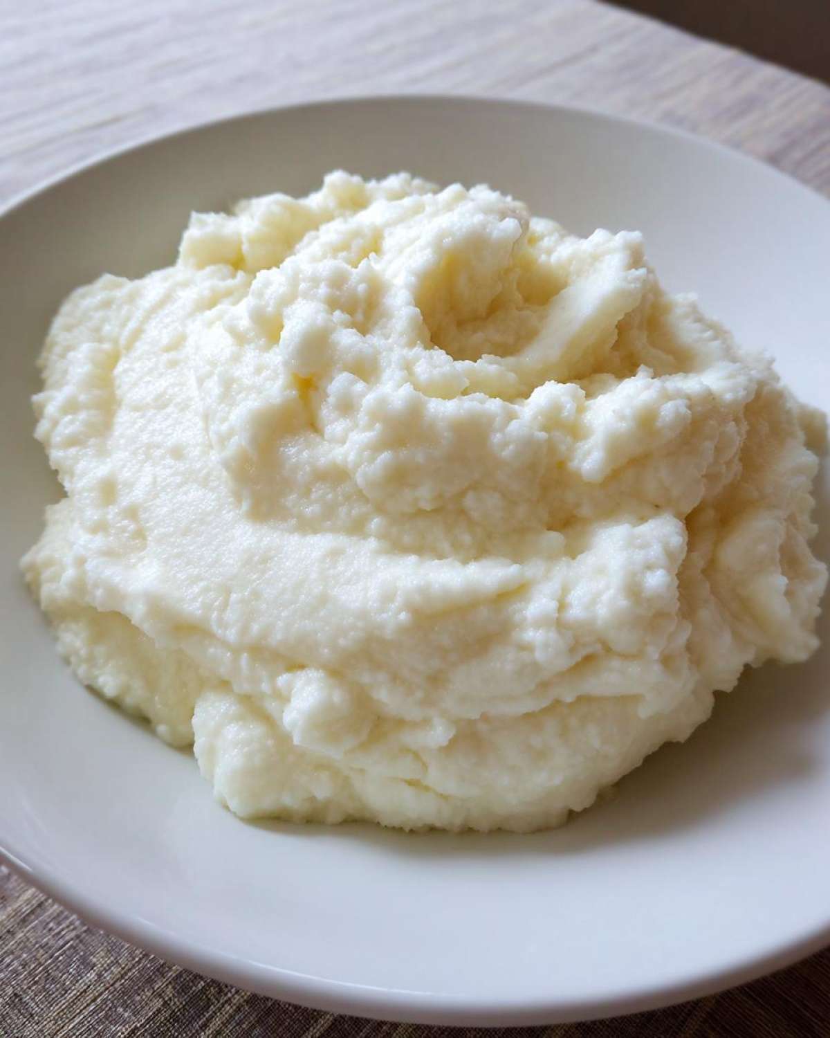 A close-up of fluffy, white Creamy Garlic Mashed Cauliflower served in a simple white bowl.