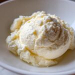 A scoop of light yellow, fluffy Creamy Garlic Mashed Cauliflower served in a white bowl.
