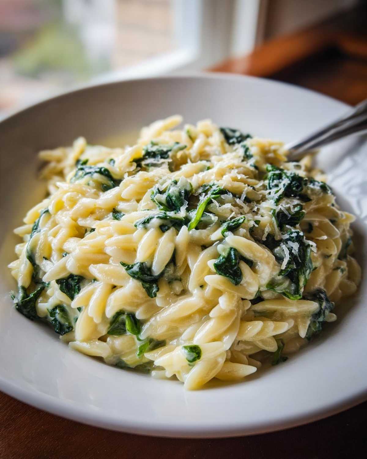 A close-up of a white bowl filled with Creamy Garlic Parmesan Orzo with Spinach, topped with grated cheese.