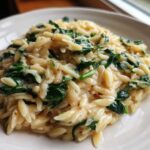 A close-up of a serving of Creamy Garlic Parmesan Orzo with Spinach, showing the creamy sauce coating the pasta and vibrant green spinach leaves.