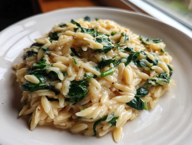 A close-up of a serving of Creamy Garlic Parmesan Orzo with Spinach, showing the creamy sauce coating the pasta and vibrant green spinach leaves.