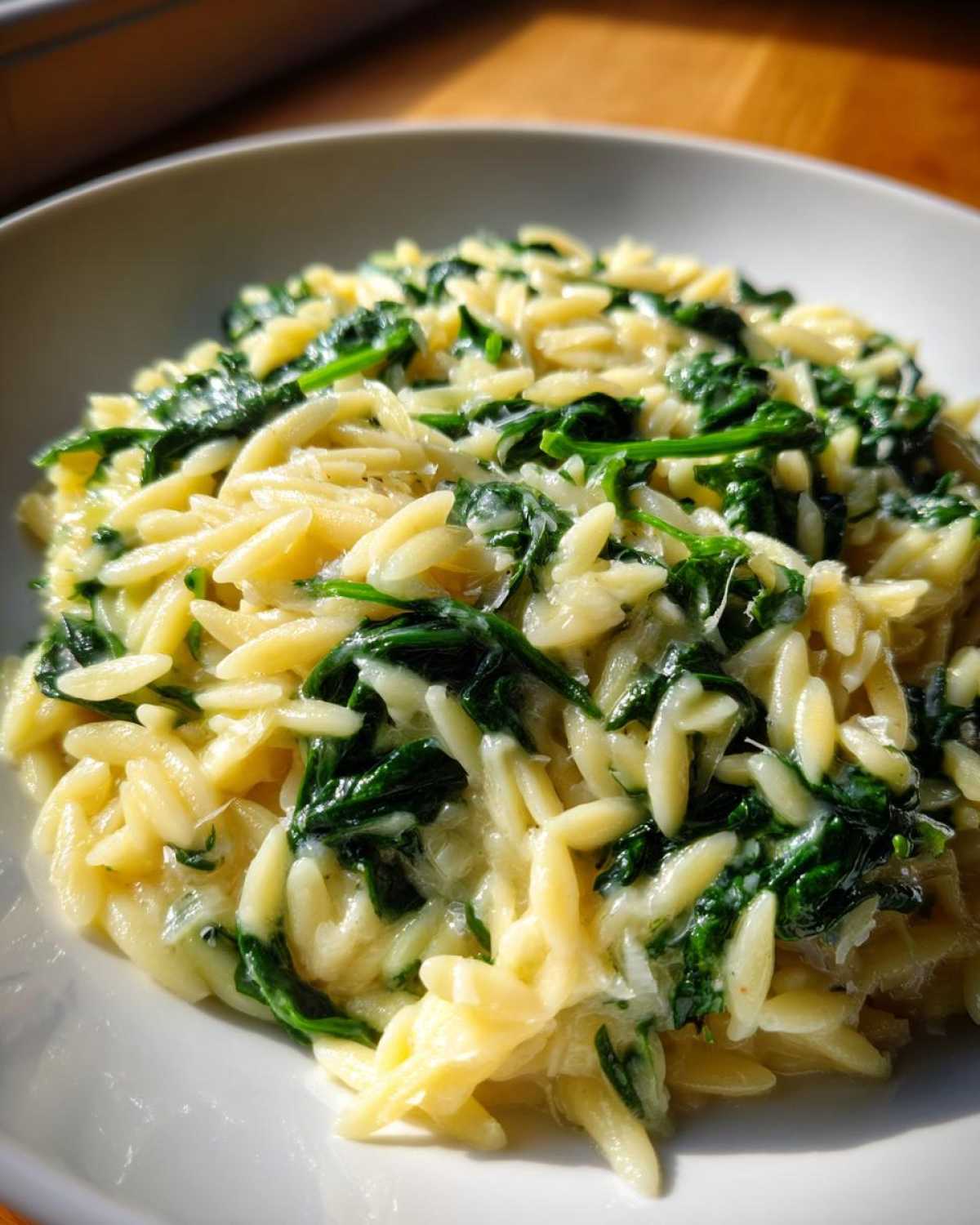 Close-up of a bowl filled with Creamy Garlic Parmesan Orzo with Spinach, showing creamy sauce and bright green wilted spinach.