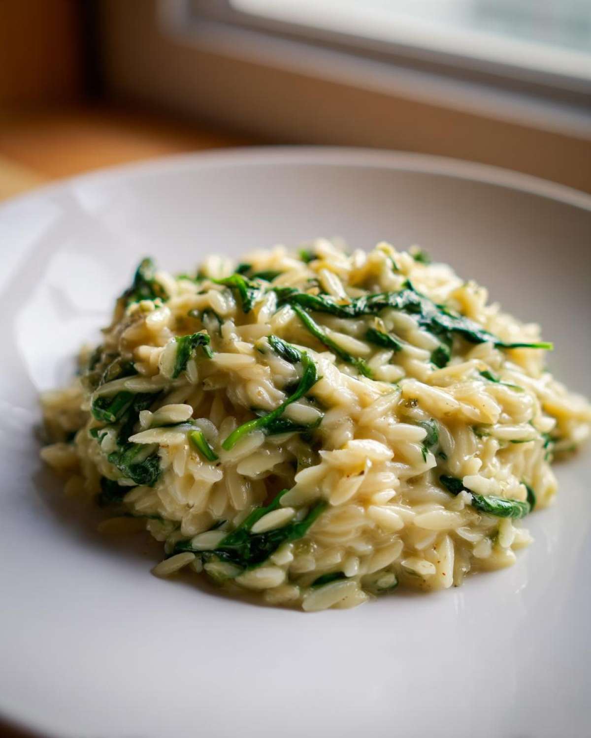 A close-up of a serving of Creamy Garlic Parmesan Orzo with Spinach on a white plate.