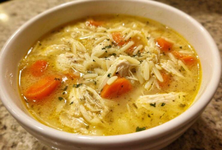 Close-up of a white bowl filled with Creamy Lemon Chicken Orzo Soup, showing shredded chicken, orzo pasta, and bright orange carrots.