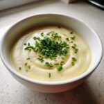 A close-up of a bowl of smooth, creamy potato leek soup topped generously with fresh chopped chives.