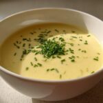 A bowl of rich, yellow Creamy Potato Leek Soup topped generously with fresh chopped chives.