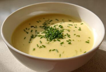A bowl of rich, yellow Creamy Potato Leek Soup topped generously with fresh chopped chives.