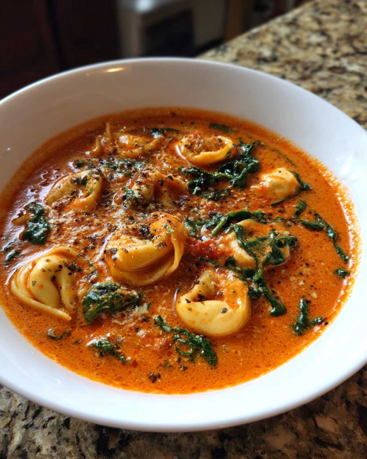 Close-up of a white bowl filled with Creamy Tomato Tortellini Soup, featuring tortellini, spinach, and grated cheese.