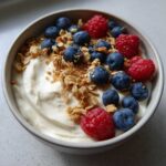 Close-up of a Creamy Vanilla Protein Smoothie Bowl topped with fresh blueberries, raspberries, and granola.