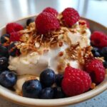 Close-up of a Creamy Vanilla Protein Smoothie Bowl topped with fresh raspberries, blueberries, and granola.