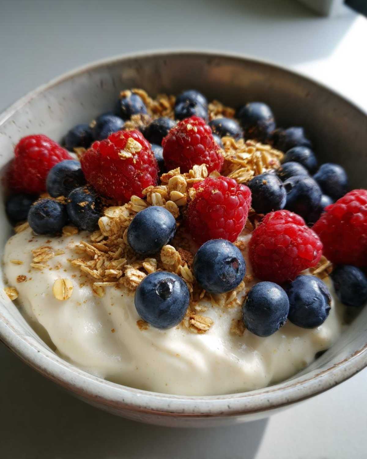 Close-up of a thick Creamy Vanilla Protein Smoothie Bowl topped with fresh raspberries, blueberries, and granola.