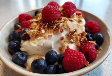 Close-up of a Creamy Vanilla Protein Smoothie Bowl topped with fresh raspberries, blueberries, and granola.