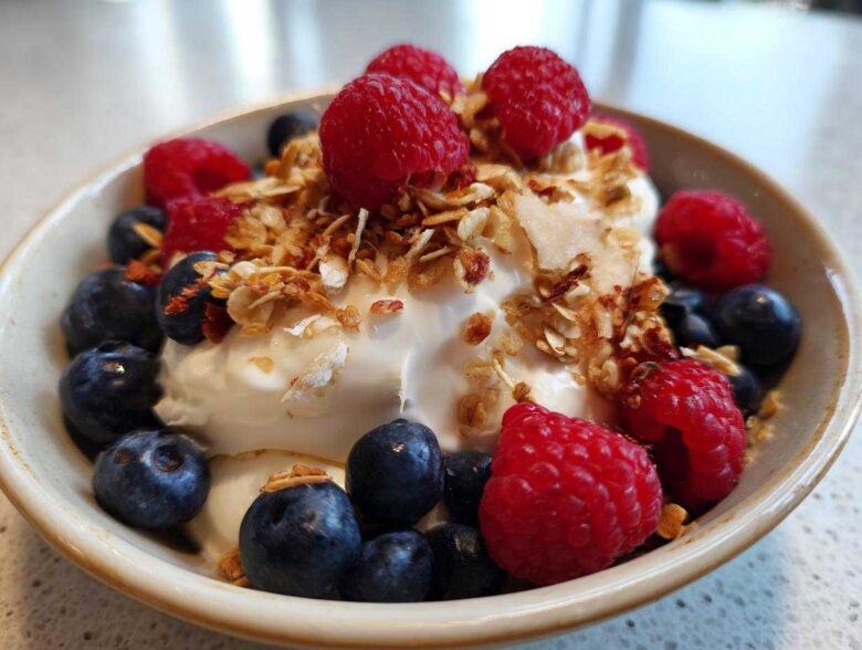 Close-up of a Creamy Vanilla Protein Smoothie Bowl topped with fresh raspberries, blueberries, and granola.