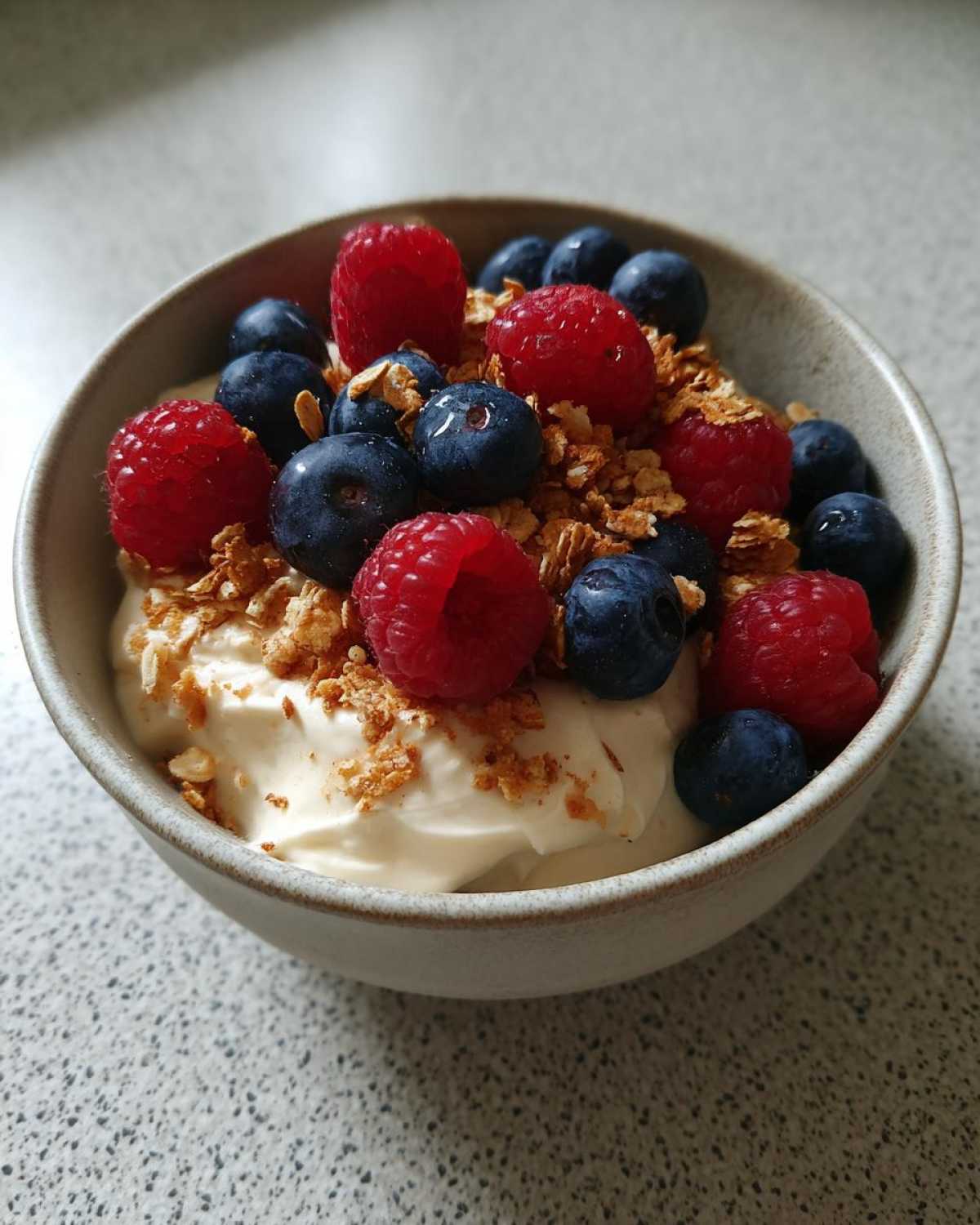 Close-up of a Creamy Vanilla Protein Smoothie Bowl topped with fresh raspberries, blueberries, and granola.