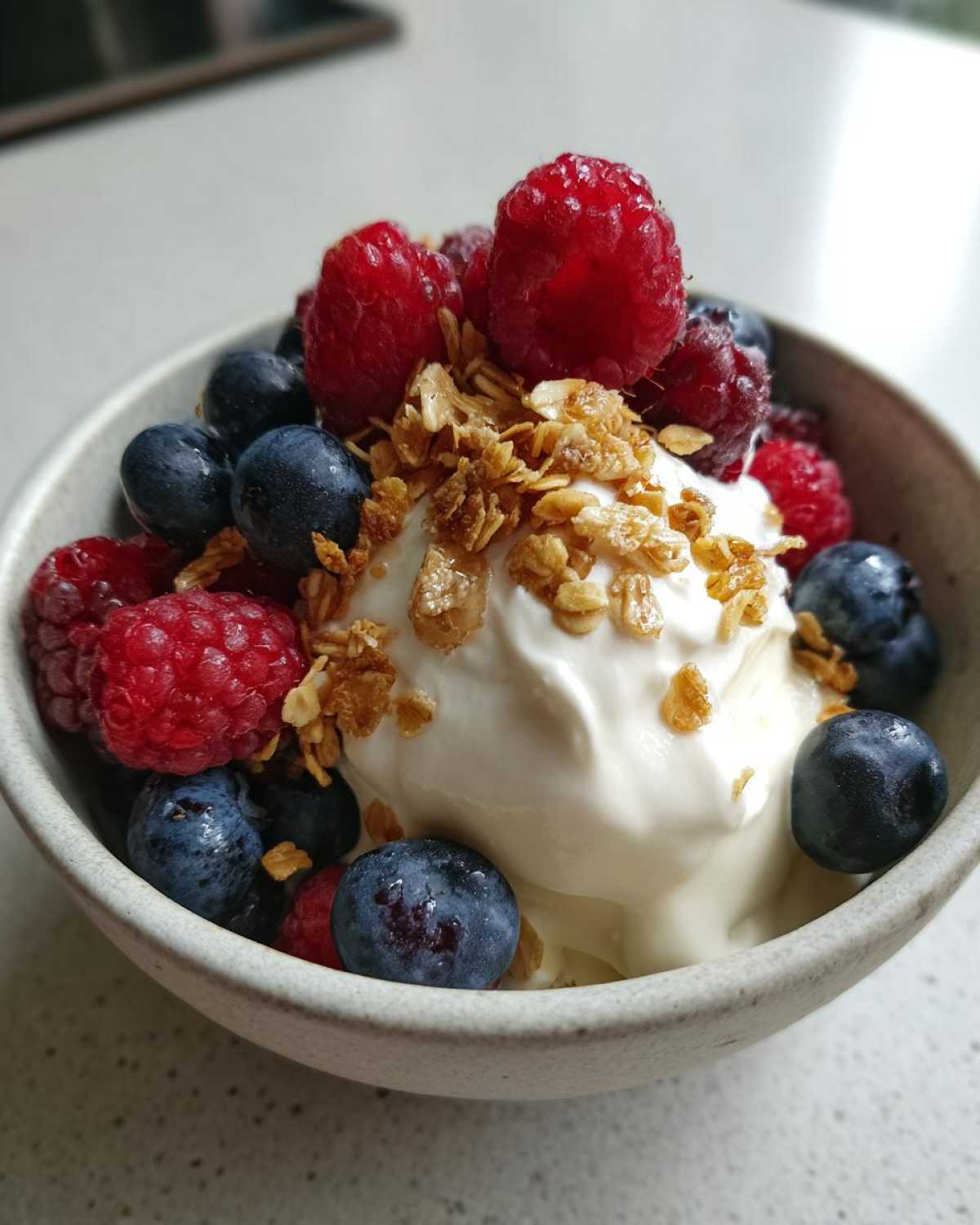 Close-up of a Creamy Vanilla Protein Smoothie Bowl topped with fresh raspberries, blueberries, and granola.