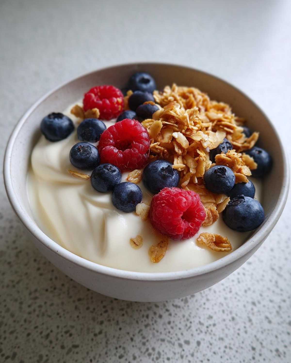 Close-up of a Creamy Vanilla Protein Smoothie Bowl topped with fresh raspberries, blueberries, and granola.