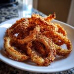 A close-up of perfectly crispy, golden-brown Air Fryer Onion Rings piled on a white plate.