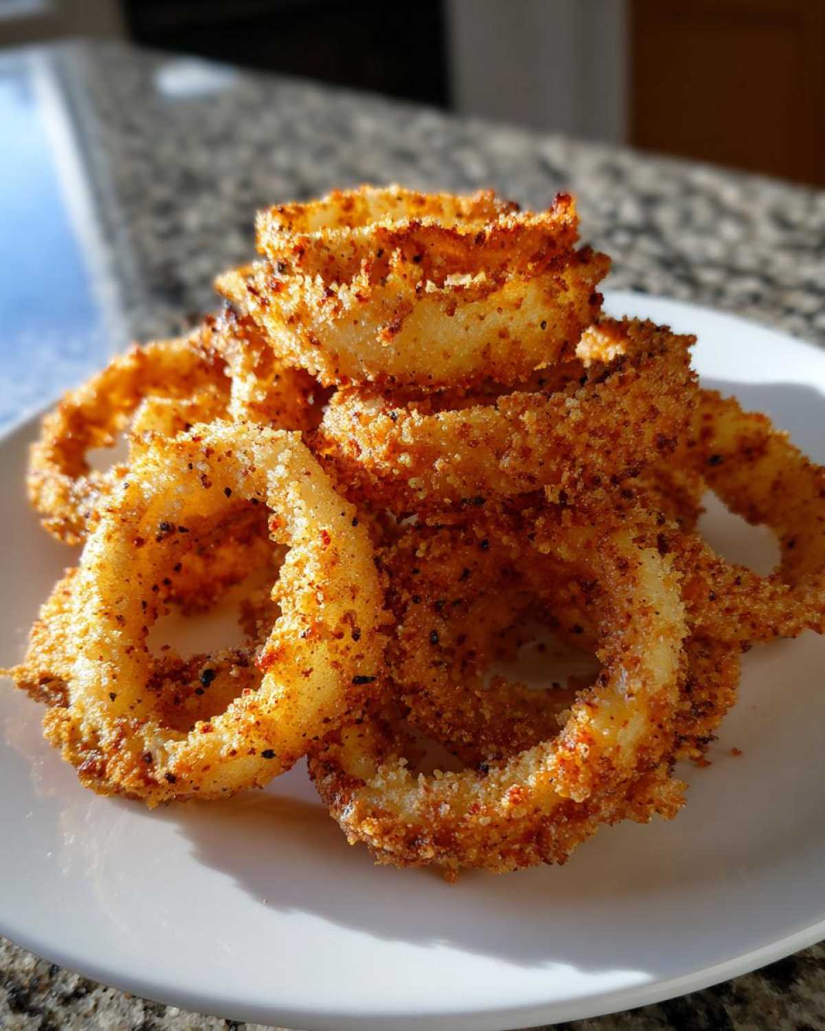 A close-up stack of perfectly golden and crispy Air Fryer Onion Rings seasoned with spices on a white plate.
