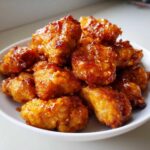 Close-up of crispy, glazed pieces of Air Fryer Orange Chicken piled high on a white plate.