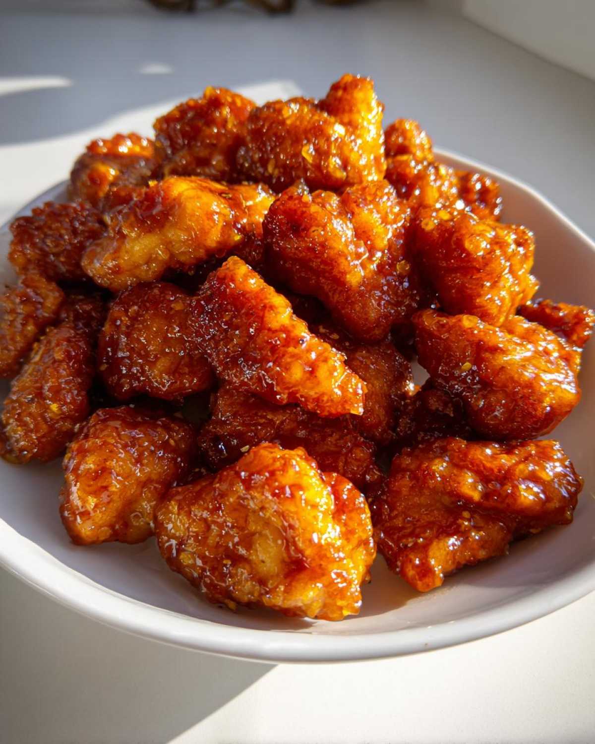 Close-up of crispy, glazed pieces of Air Fryer Orange Chicken piled high in a white bowl.