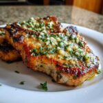 Close-up of juicy, crispy air fryer pork chops smothered in garlic butter and fresh parsley.