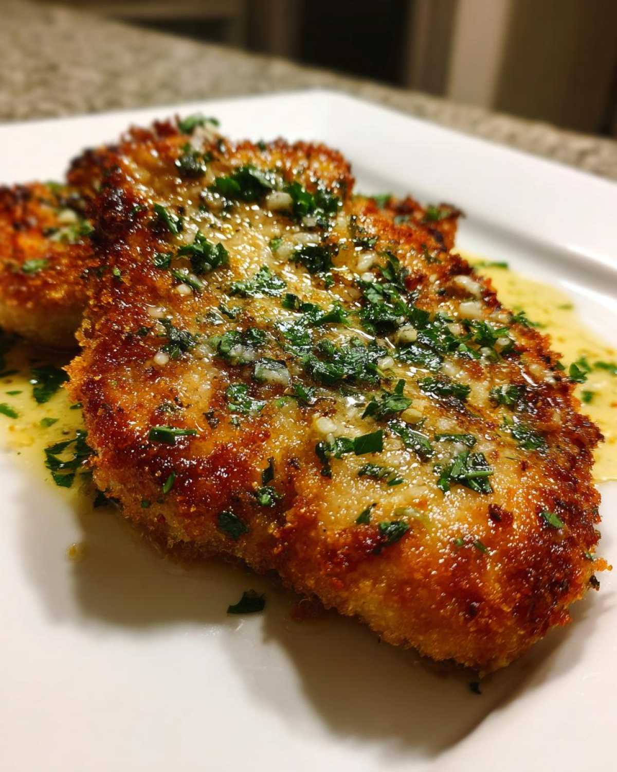 Close-up of golden brown Crispy Air Fryer Pork Chops topped with melted garlic butter and fresh parsley.