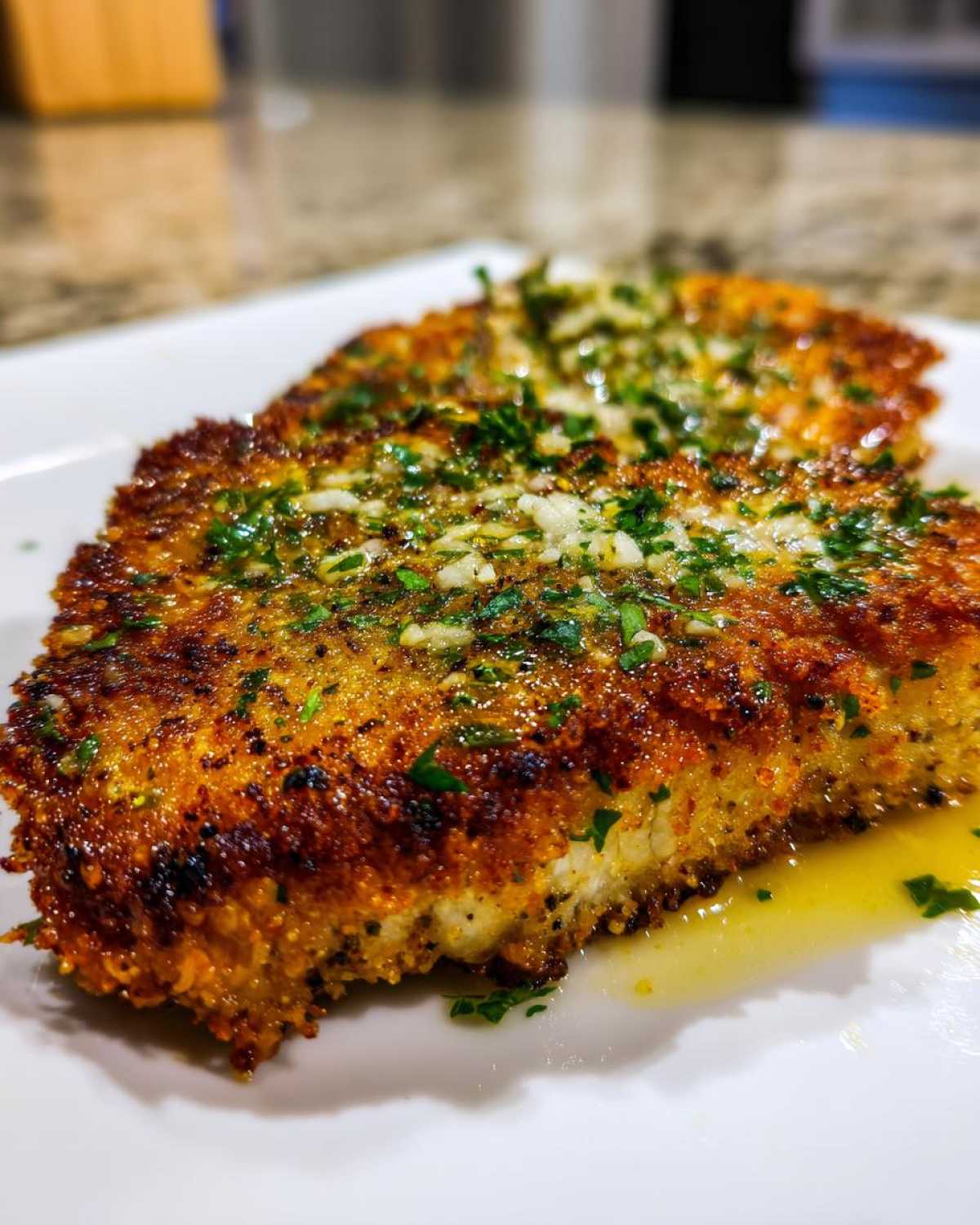 Close-up of a golden brown, crispy air fryer pork chop topped with minced garlic and fresh parsley.