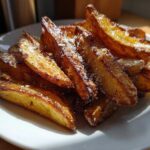 A close-up of golden brown, crispy baked garlic parmesan potato wedges piled on a white plate.