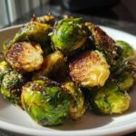 A close-up of roasted Crispy Parmesan Brussels Sprouts showing browned edges and melted cheese in a white bowl.