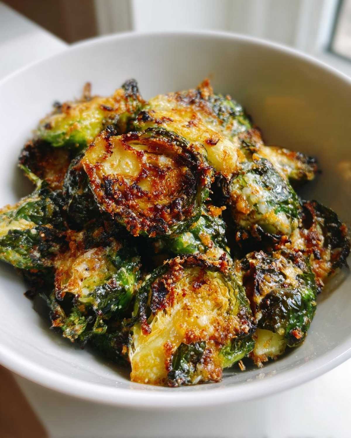 Close-up of deeply roasted Crispy Parmesan Brussels Sprouts in a white bowl.