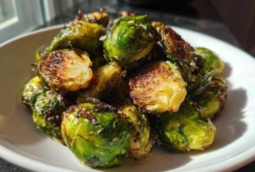 A close-up of roasted Crispy Parmesan Brussels Sprouts showing browned edges and melted cheese in a white bowl.