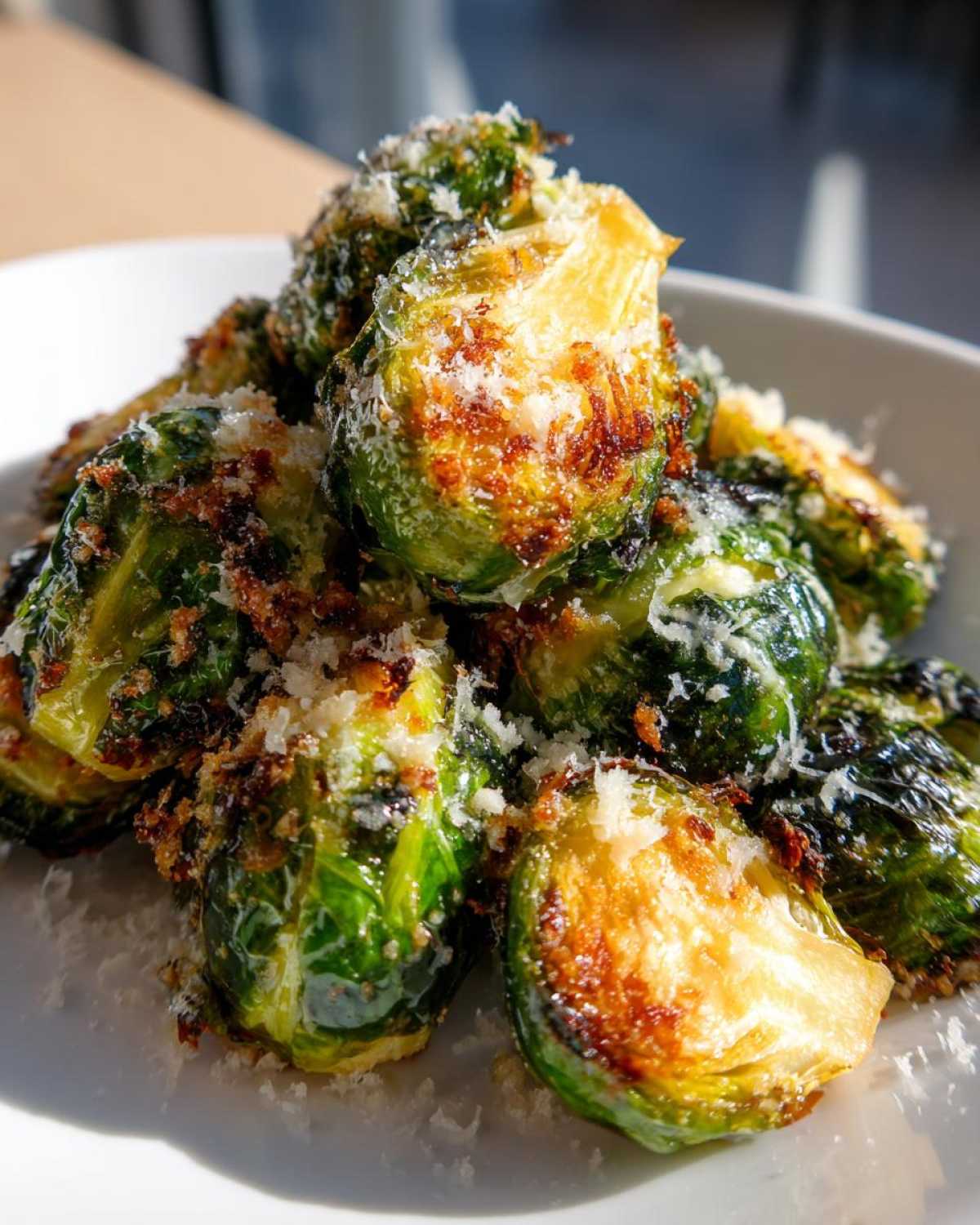 A close-up of roasted, crispy Parmesan Brussels Sprouts piled high on a white plate.