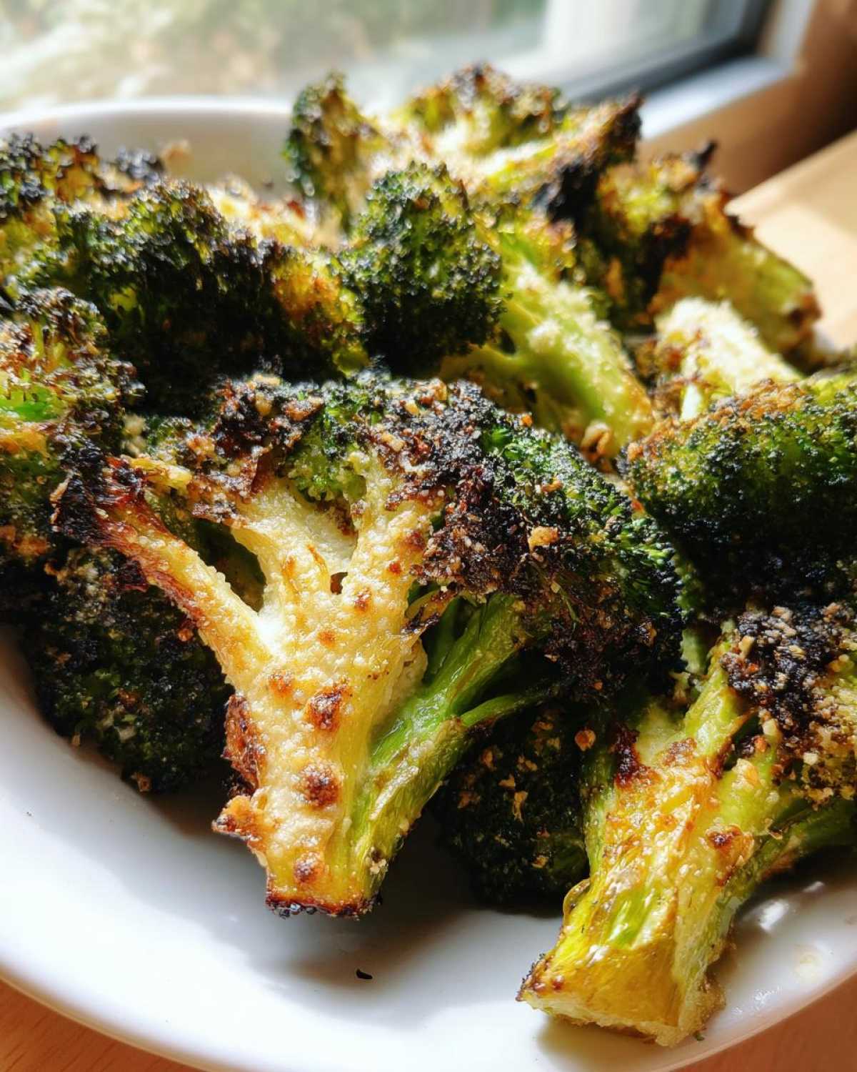 Close-up of intensely roasted, charred, and cheesy Crispy Parmesan Roasted Broccoli florets served on a white plate.