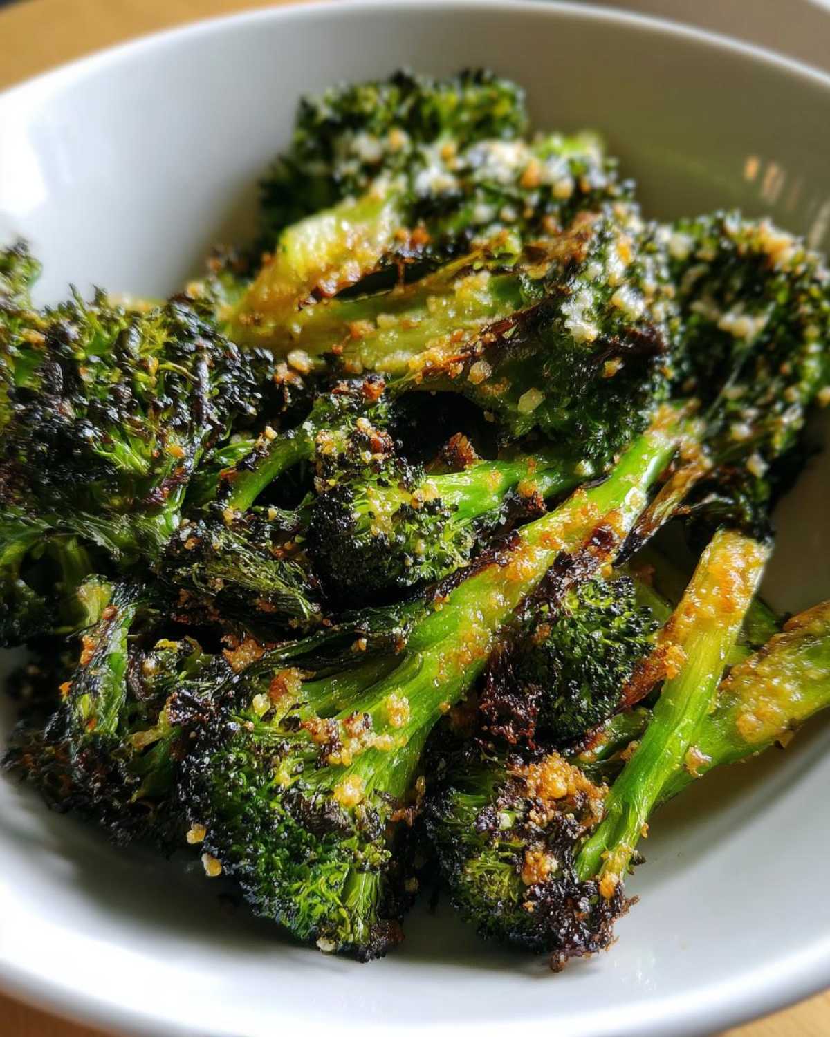 A close-up shot of perfectly roasted, dark green Crispy Parmesan Roasted Broccoli florets in a white bowl.