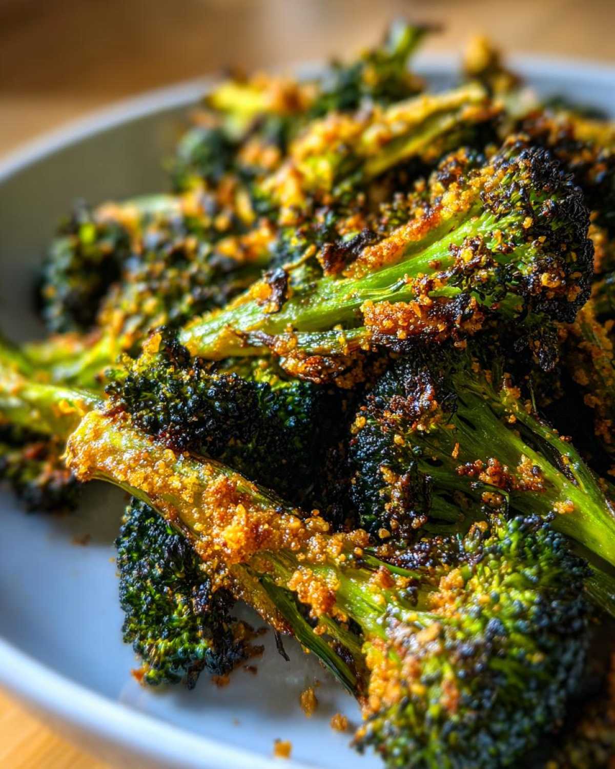 Close-up of bright green and charred Crispy Parmesan Roasted Broccoli florets piled high on a white plate.
