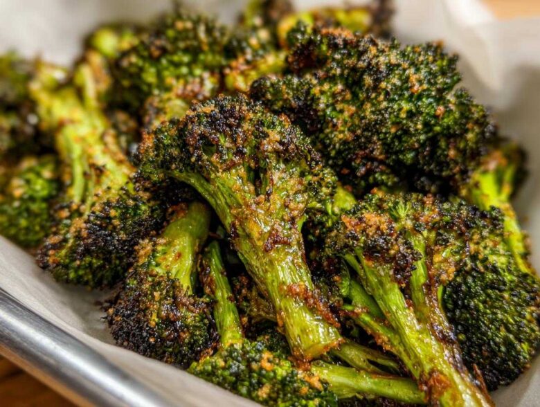 Close-up of deeply roasted, dark green broccoli florets coated in crispy Parmesan cheese.