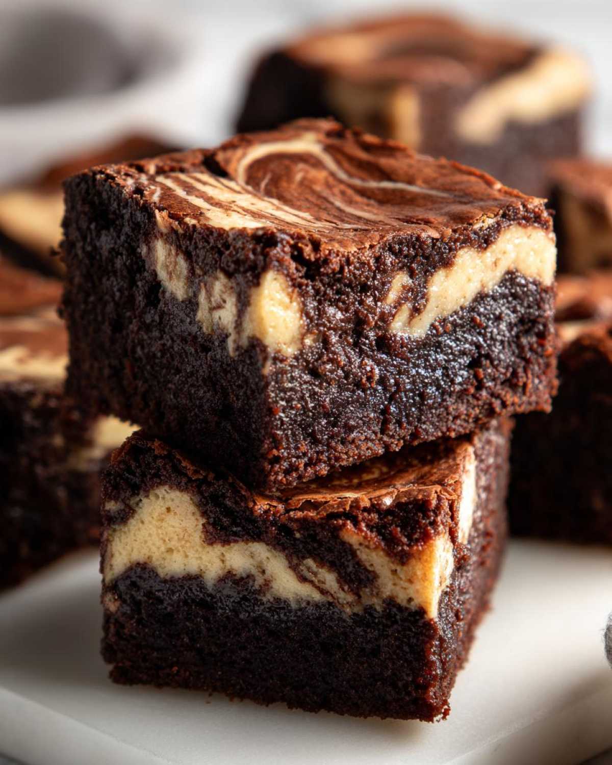 Two stacked, fudgy Dark Chocolate Tahini Brownies with a beautiful light-colored tahini swirl on top.