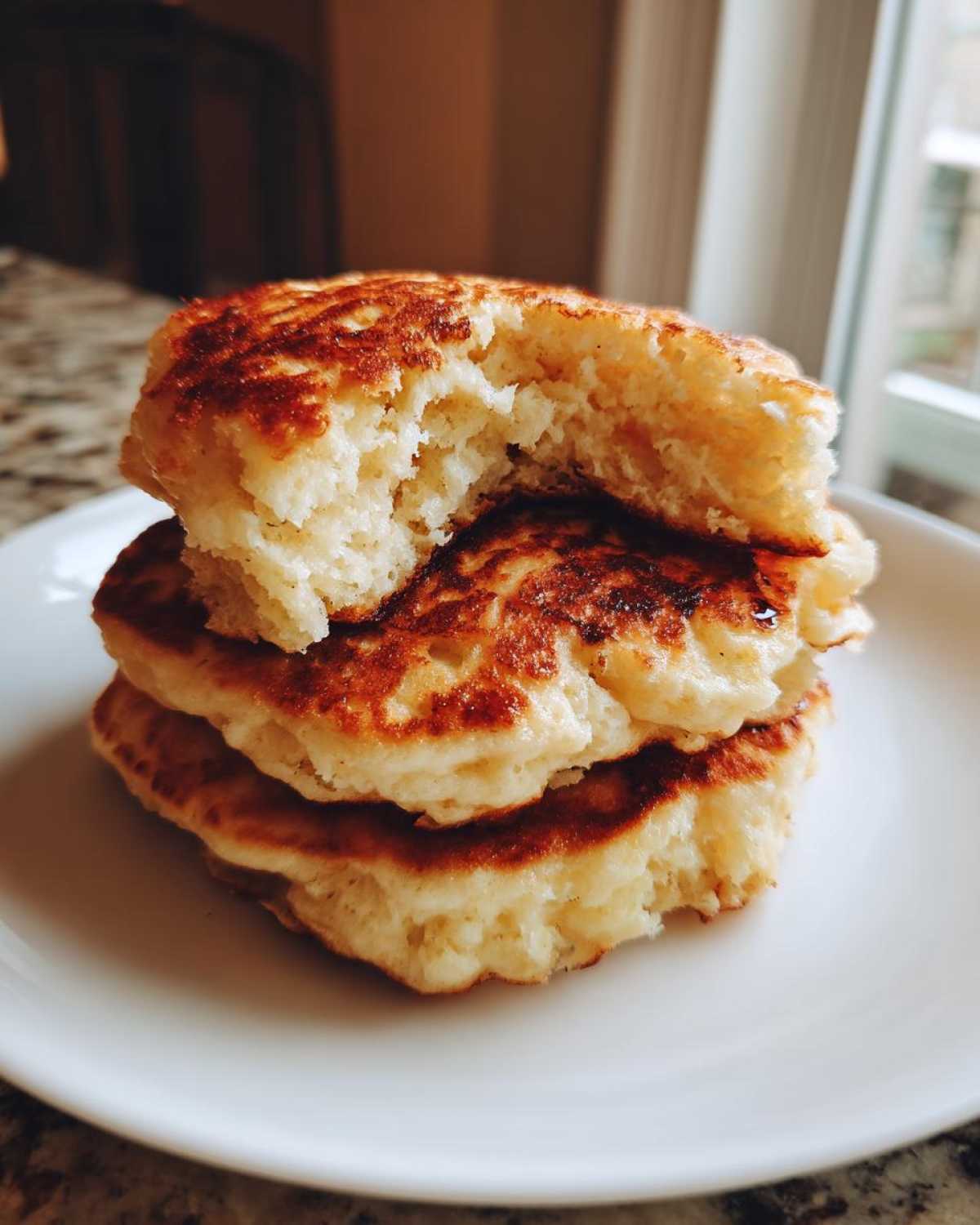 Close-up of a stack of three fluffy Gluten-Free Buttermilk Pancakes, with the top one broken open showing the airy interior.