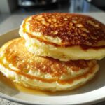 Close-up of two thick, fluffy Lemon Ricotta Pancakes stacked on a white plate with syrup pooling underneath.