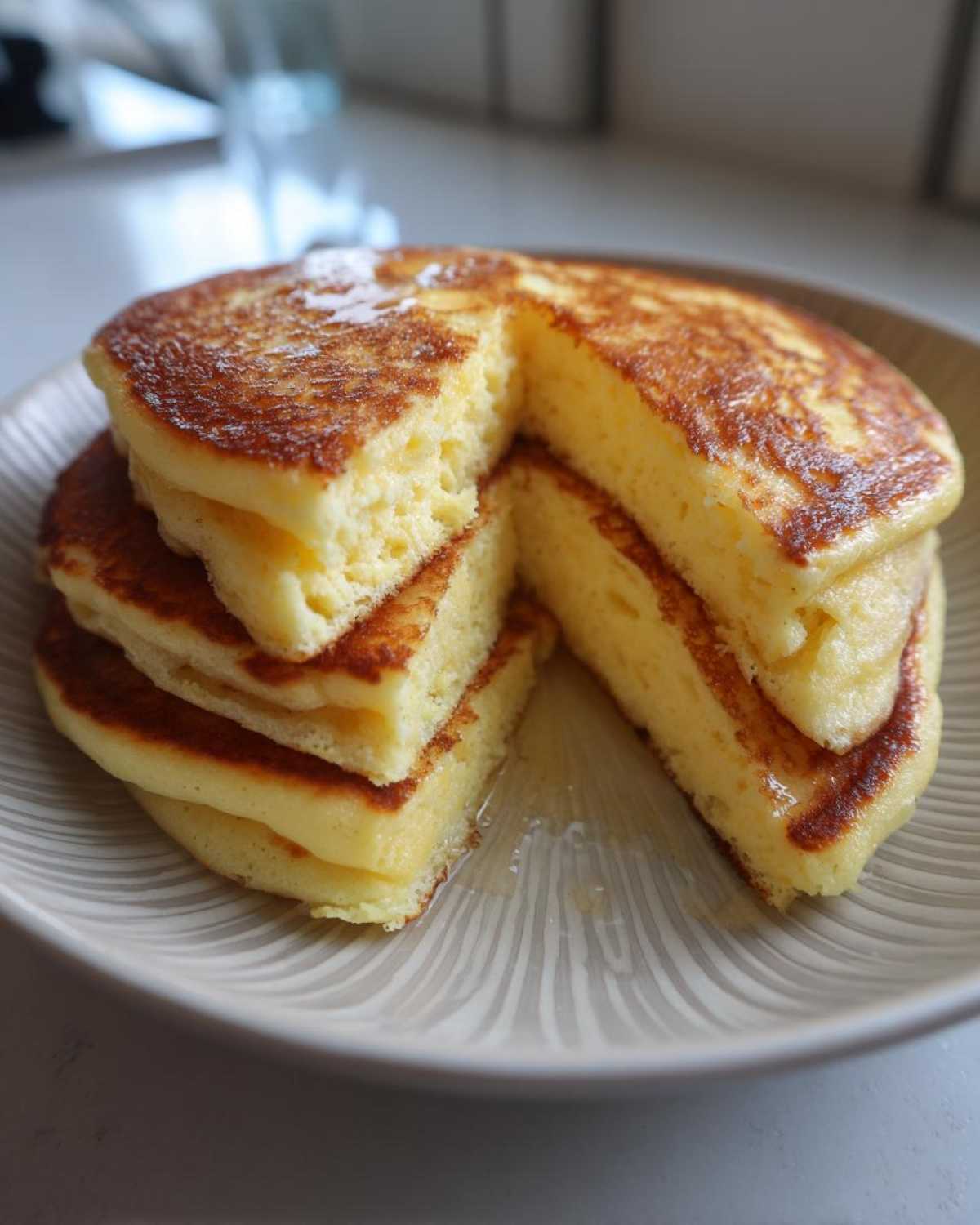 A stack of thick, fluffy Lemon Ricotta Pancakes cut to show the airy interior, drizzled with syrup.