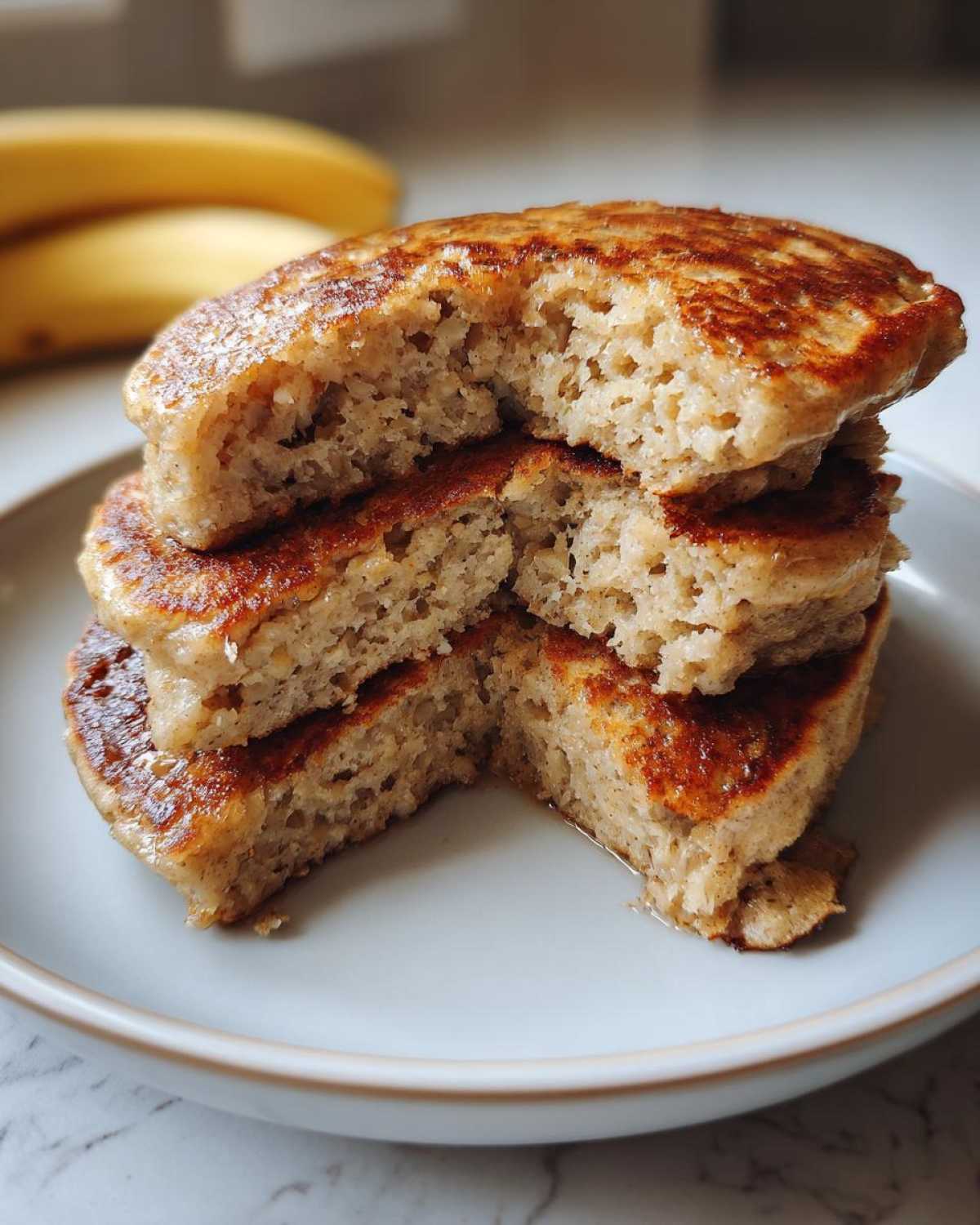 Close-up of a stack of fluffy Vegan Banana Oat Pancakes with a bite taken out, showing the oat texture inside.